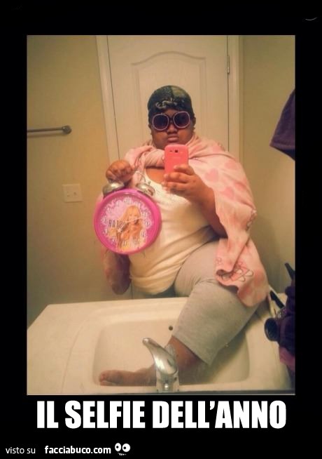 Il selfie dell'anno. Ragazzo ciccione con copertina mantello e sveglia rosa con un piede dentro il lavabo